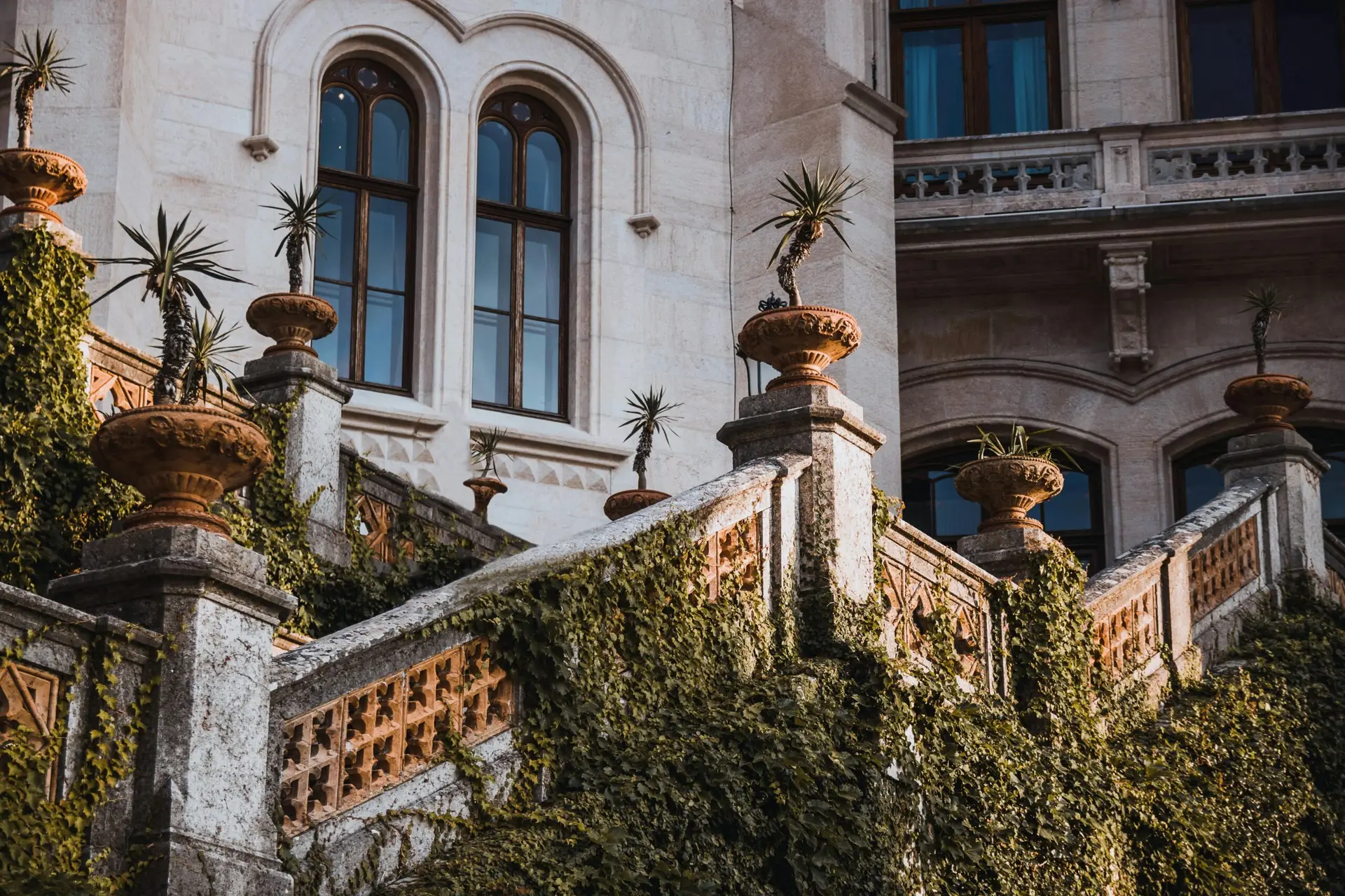 Historic villa exterior with ivy-clad stone staircase and potted plants.